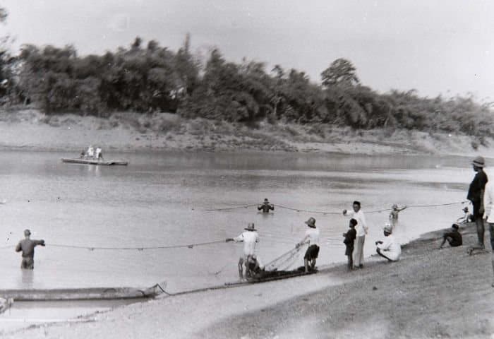 Kegiatan menangkap ikan di tepi sungai dengan perahu dan jaring.